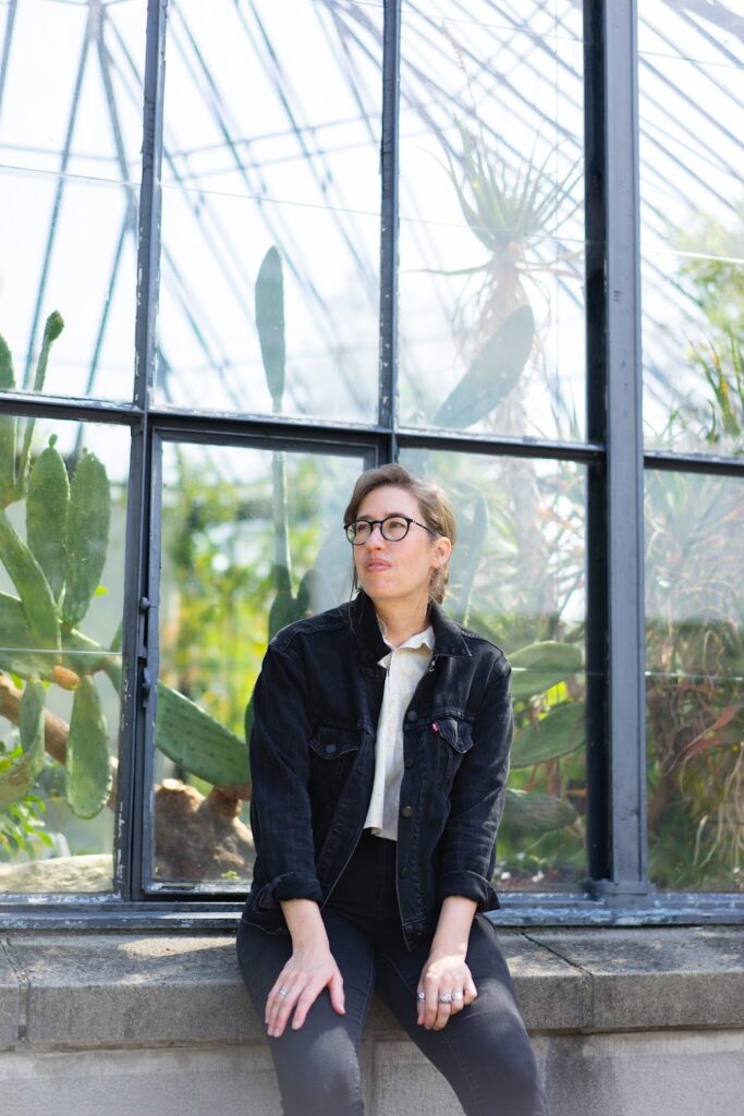 Photograph of Kit Anderson, sitting on a window ledge of a green house.